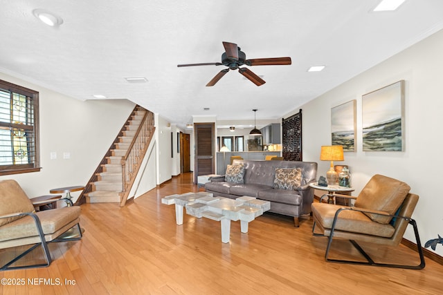 living area with a ceiling fan, wood finished floors, crown molding, and stairs