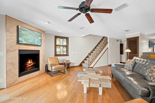 living room featuring visible vents, hardwood / wood-style flooring, ornamental molding, stairs, and a fireplace