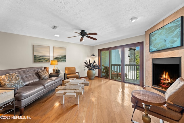 living area with visible vents, ceiling fan, hardwood / wood-style floors, a lit fireplace, and a textured ceiling