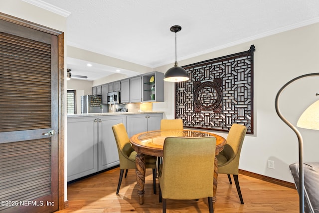 dining area with ornamental molding, a ceiling fan, light wood-style flooring, and baseboards