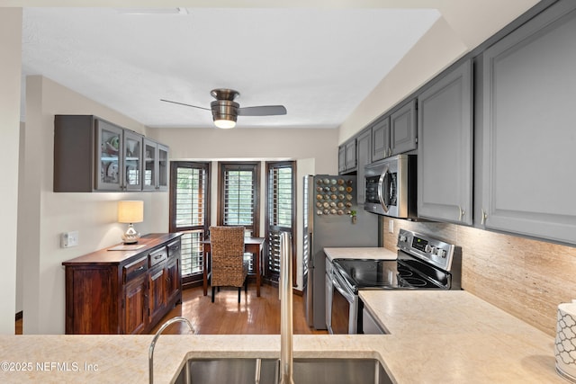 kitchen with stainless steel appliances, wood finished floors, light countertops, backsplash, and glass insert cabinets