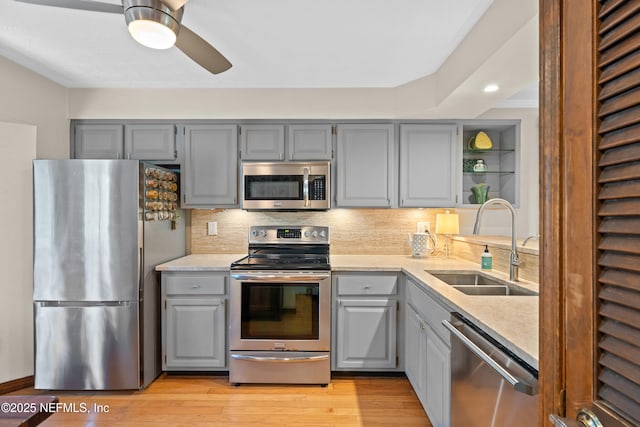 kitchen featuring stainless steel appliances, tasteful backsplash, gray cabinetry, a sink, and light wood-type flooring