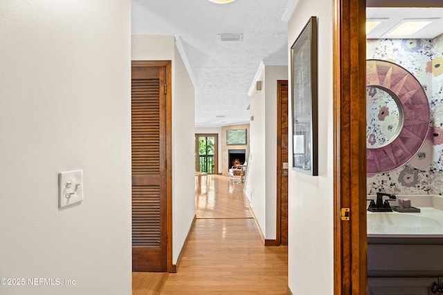 corridor featuring light wood-style flooring, ornamental molding, a sink, a textured ceiling, and baseboards