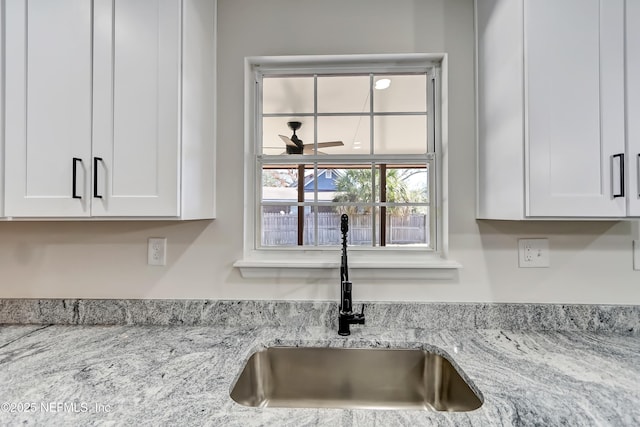 room details with white cabinetry, sink, and light stone countertops