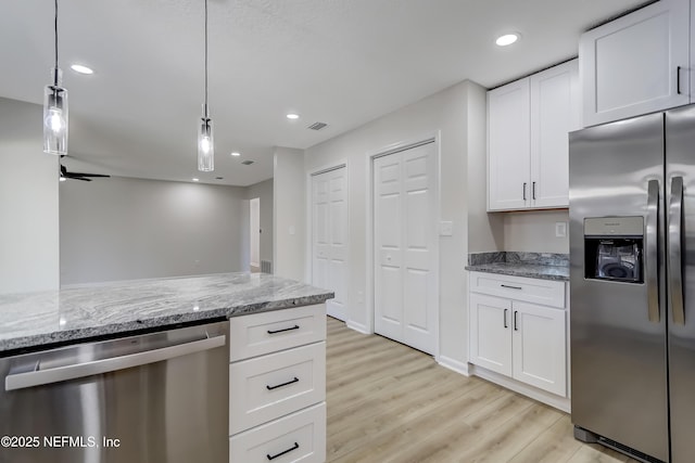 kitchen featuring appliances with stainless steel finishes, pendant lighting, white cabinets, light stone counters, and light hardwood / wood-style floors