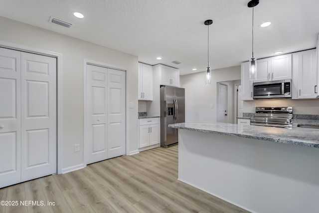 kitchen featuring light stone counters, decorative light fixtures, appliances with stainless steel finishes, light hardwood / wood-style floors, and white cabinets