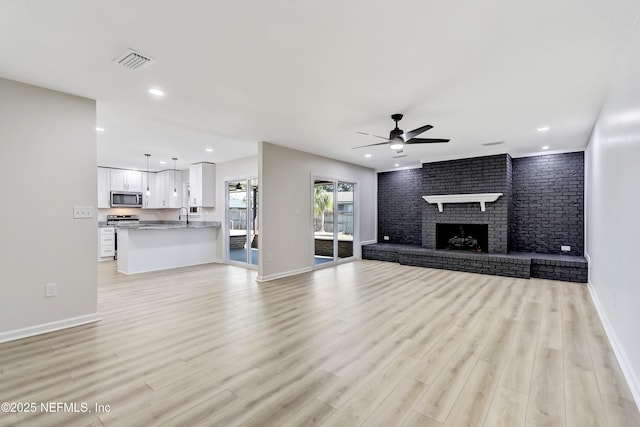 unfurnished living room featuring brick wall, sink, ceiling fan, a brick fireplace, and light wood-type flooring