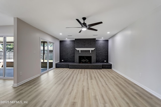 unfurnished living room featuring brick wall, ceiling fan, a brick fireplace, and light wood-type flooring