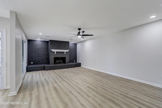 unfurnished living room featuring light hardwood / wood-style flooring, a fireplace, ceiling fan, and brick wall