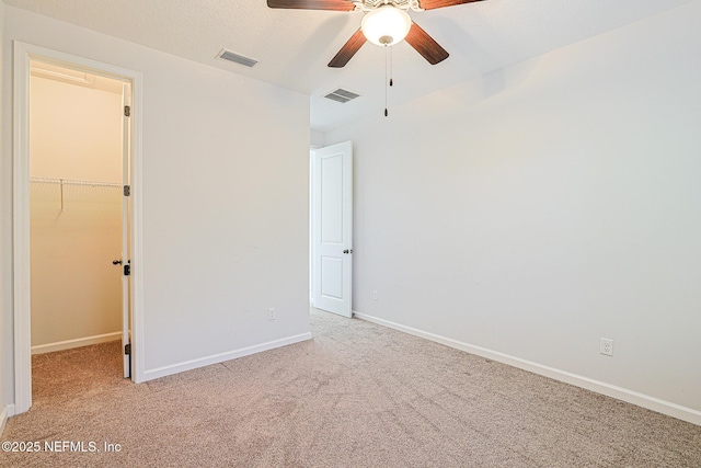 unfurnished bedroom featuring a walk in closet, light carpet, a closet, and ceiling fan