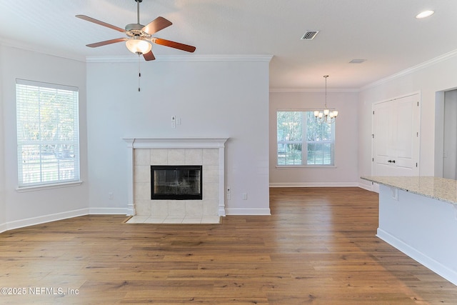 unfurnished living room featuring ceiling fan with notable chandelier, hardwood / wood-style flooring, a tiled fireplace, and crown molding