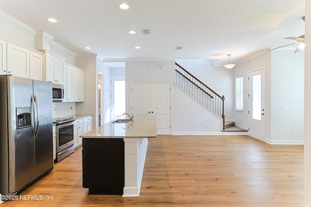 kitchen with light stone countertops, a center island with sink, backsplash, white cabinets, and appliances with stainless steel finishes