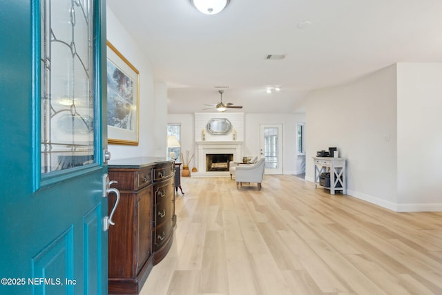 foyer entrance featuring ceiling fan, a fireplace, and light hardwood / wood-style flooring