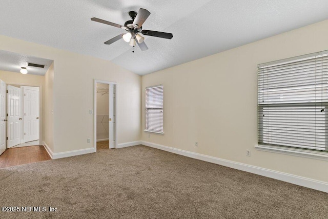 unfurnished bedroom with vaulted ceiling, a walk in closet, carpet floors, a closet, and ceiling fan