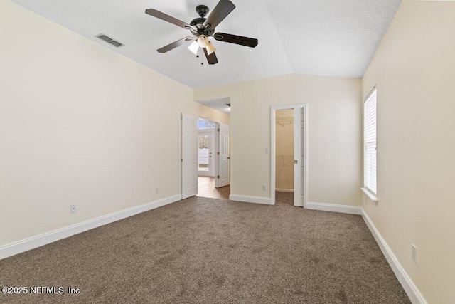 unfurnished bedroom featuring a walk in closet, carpet floors, a closet, vaulted ceiling, and ceiling fan