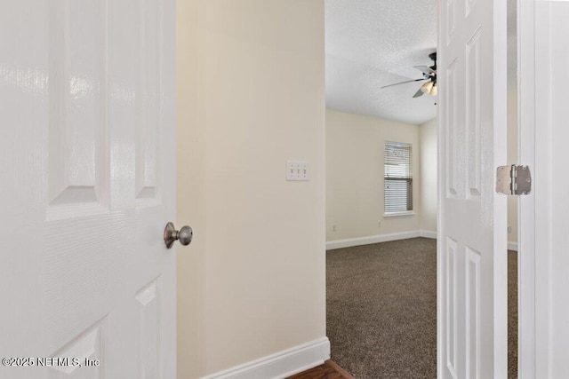 hallway with a textured ceiling and dark colored carpet