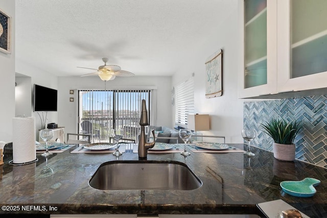 kitchen featuring decorative backsplash, sink, ceiling fan, and dark stone countertops