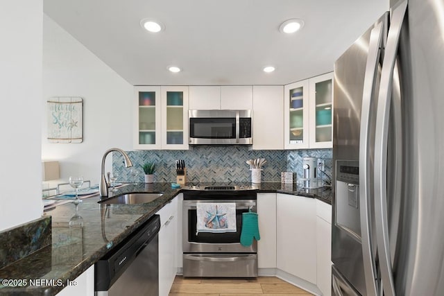 kitchen featuring stainless steel appliances, white cabinetry, dark stone counters, and sink