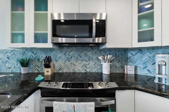 kitchen with white cabinets, stainless steel appliances, dark stone counters, and tasteful backsplash