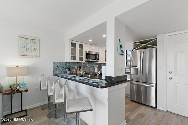 kitchen with white cabinetry, kitchen peninsula, appliances with stainless steel finishes, light wood-type flooring, and a breakfast bar