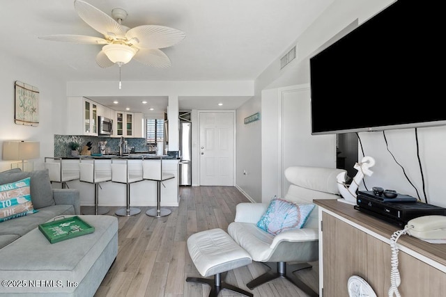 living room with ceiling fan, light hardwood / wood-style floors, and sink