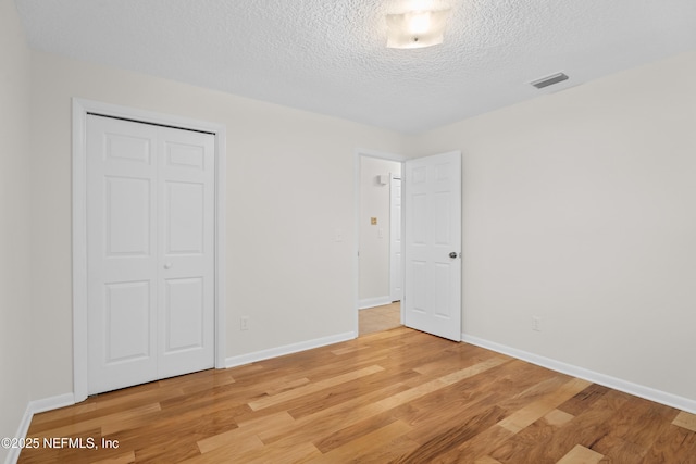 unfurnished bedroom featuring a textured ceiling, light wood-type flooring, and a closet