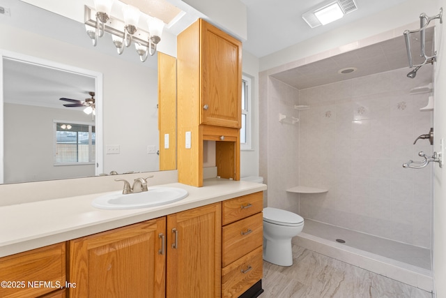 bathroom with a tile shower, ceiling fan, vanity, and toilet