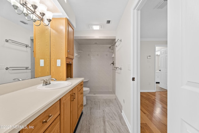 bathroom featuring a tile shower, vanity, toilet, and crown molding