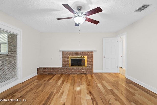 unfurnished living room featuring hardwood / wood-style flooring, ceiling fan, a textured ceiling, and a brick fireplace