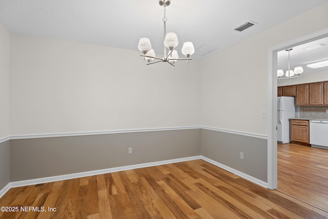 unfurnished dining area featuring a textured ceiling, light hardwood / wood-style floors, and a notable chandelier