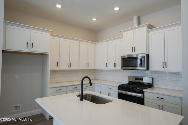 kitchen with a kitchen island with sink, backsplash, white cabinetry, appliances with stainless steel finishes, and sink