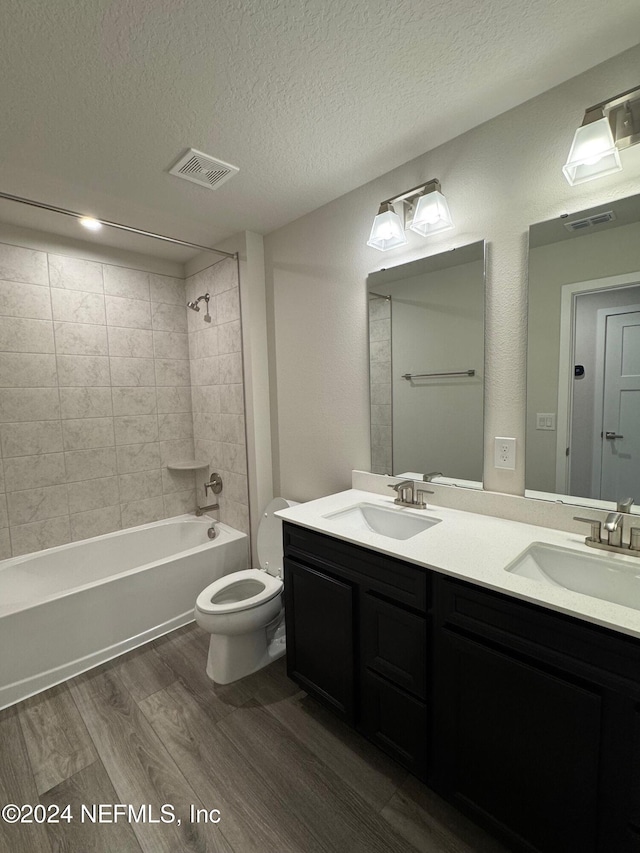 full bathroom featuring vanity, tiled shower / bath combo, a textured ceiling, hardwood / wood-style floors, and toilet