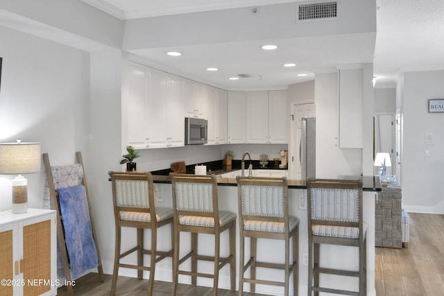 2003 Windjammer Ln, Saint Augustine, FL 32084 - kitchen with appliances with stainless steel finishes, crown molding, kitchen peninsula, a kitchen bar, and white cabinetry