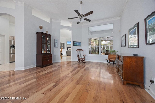 interior space with ceiling fan, a high ceiling, crown molding, and light wood-type flooring