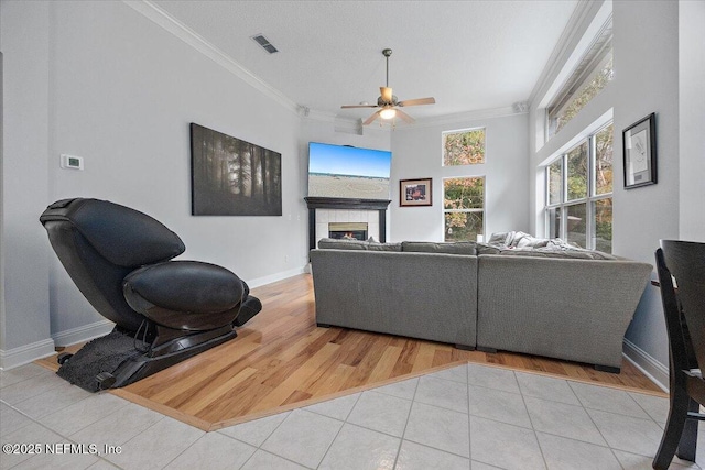 tiled living room with ceiling fan, a fireplace, and crown molding