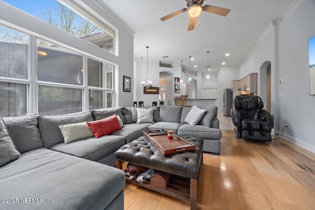 living room with ceiling fan with notable chandelier, ornamental molding, and light hardwood / wood-style floors