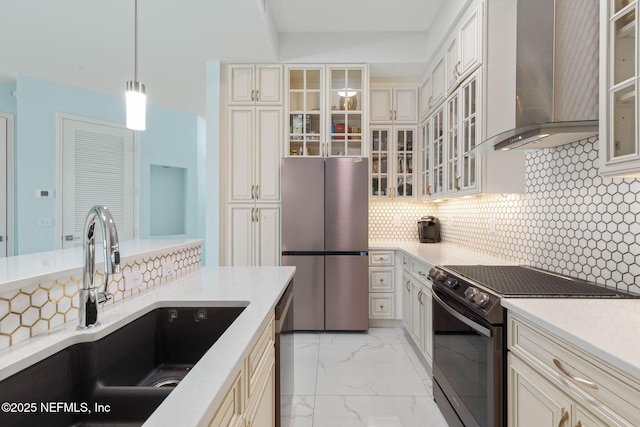 kitchen featuring electric range oven, wall chimney range hood, sink, pendant lighting, and stainless steel refrigerator