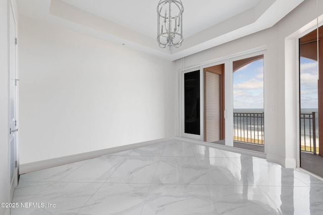 spare room with a chandelier, a tray ceiling, and a water view