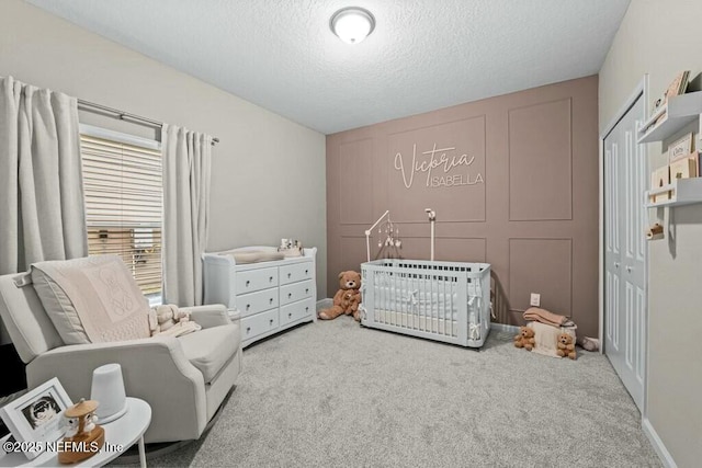 bedroom featuring a textured ceiling, a closet, light colored carpet, and a crib