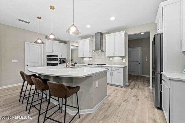 kitchen with white cabinets, appliances with stainless steel finishes, wall chimney range hood, an island with sink, and sink