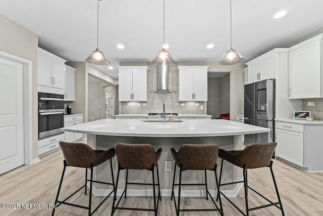 kitchen with decorative light fixtures, wall chimney range hood, and white cabinets