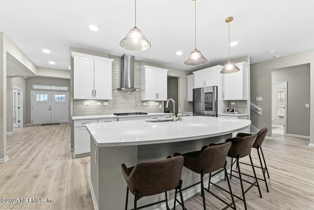 kitchen featuring white cabinetry, wall chimney range hood, pendant lighting, and stainless steel refrigerator