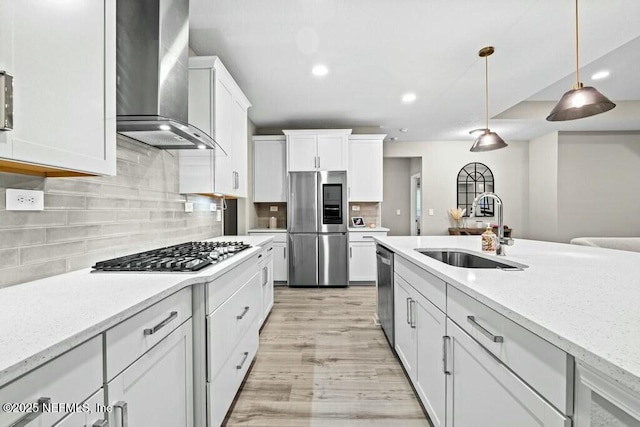 kitchen with wall chimney range hood, sink, hanging light fixtures, stainless steel appliances, and light stone counters