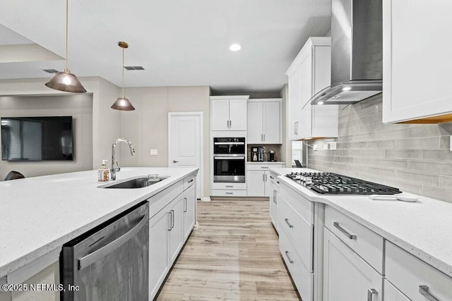 kitchen featuring wall chimney range hood, sink, hanging light fixtures, stainless steel appliances, and white cabinets