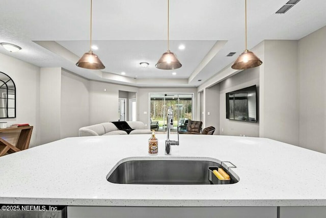 kitchen with a raised ceiling, decorative light fixtures, sink, and a kitchen island with sink