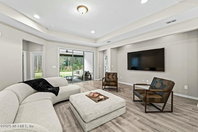 living room with a textured ceiling, light hardwood / wood-style floors, and a raised ceiling