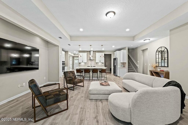 living room featuring a textured ceiling, a raised ceiling, and light wood-type flooring