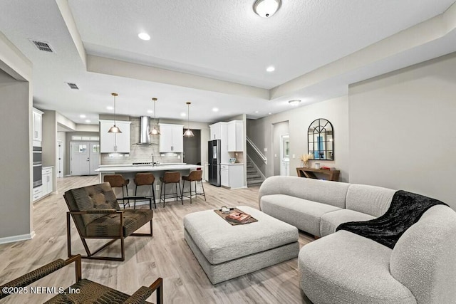 living room featuring sink, a tray ceiling, and light wood-type flooring