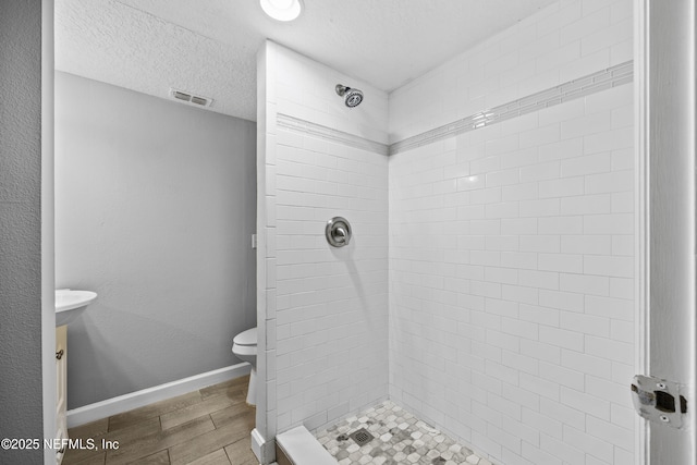 bathroom featuring tiled shower, a textured ceiling, and toilet