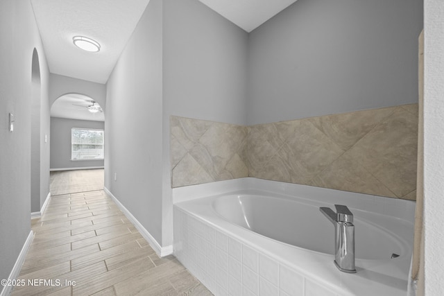 bathroom featuring ceiling fan and a relaxing tiled tub